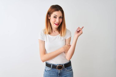 Güzel kızıl saçlı kadın yüzünde büyük bir gülümseme ile izole beyaz arka plan üzerinde duran rahat t-shirt giyen, kameraya bakarak yan el ve parmak ile işaret.