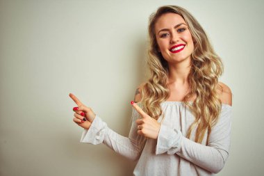 Genç güzel kadın beyaz izole arka plan üzerinde duran gülümseyerek ve yan iki el ve parmakları ile işaret kamera bakıyor.