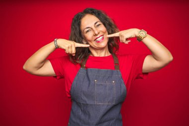 Orta yaş yaşlı kadın kırmızı izole arka plan üzerinde önlük üniforma giyen neşeli gösteren gülümseyerek ve parmakları diş ve ağız ile işaret. Diş sağlığı kavramı.