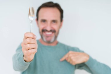 Kendini işaret eden sürpriz yüz ile izole arka plan üzerinde gümüş çatal tutan Kıdemli adam