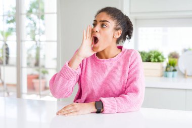 Afro saçlı güzel afro-amerikan kadın rahat pembe kazak giyen bağırarak ve ağızda el ile yan yüksek sesle bağırıyor. İletişim kavramı.