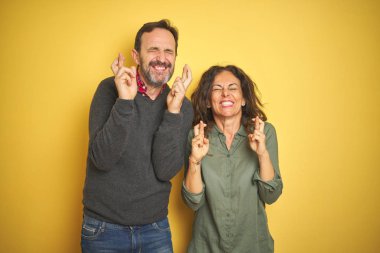 Izole sarı arka plan gesturing parmak üzerinde Güzel orta yaş çift umut ve gözleri kapalı gülümseyerek geçti. Şans ve batıl kavram.