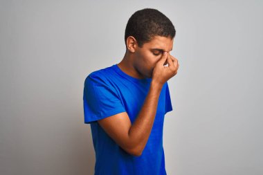 Izole beyaz arka plan yorgun sürtünme burun ve gözler yorgunluk ve baş ağrısı hissi üzerinde duran mavi t-shirt giyen genç yakışıklı Arap adam. Stres ve hayal kırıklığı kavramı.