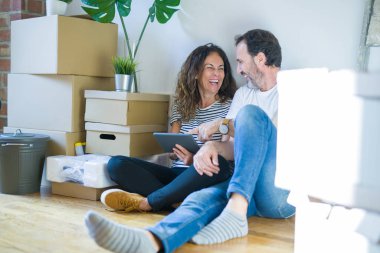 Orta yaş üst düzey romantik çift aşk etrafında kutuları ile daire katında oturan ve Touchpad tablet kullanarak yeni bir eve hareket için mutlu gülümseyen