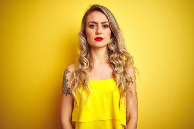 Genç attactive kadın sarı izole arka plan üzerinde duran t-shirt giyen yüzünde ciddi ifade ile rahat. Kameraya basit ve doğal bir bakış.