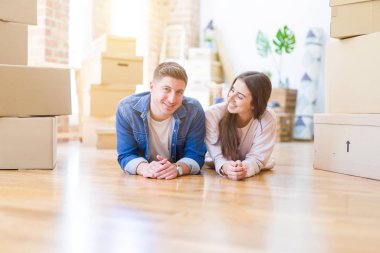Evde karton kutular etrafında yerde yatan rahatlatıcı genç güzel çift, yeni bir eve hareket mutlu gülümseyen