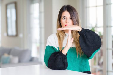 Evde kış kazak giyen genç güzel kadın elleri, sinirli ve ciddi yüz ile jest zaman dışarı yapıyor