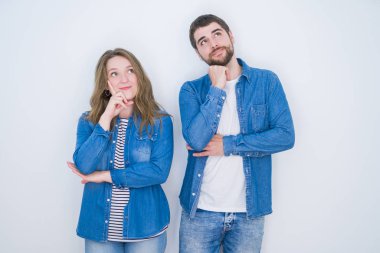 Genç güzel çift soru, dalgın ifade hakkında düşünme çene üzerinde el ile beyaz izole arka plan üzerinde birlikte ayakta. Düşünceli bir yüzle gülümsüyor. Şüphe kavramı.