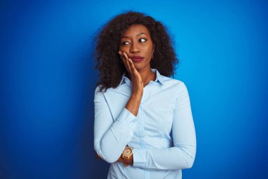 Izole mavi arka plan üzerinde duran gömlek giyen Afro-Amerikan iş kadını yorgun görünümlü ve çapraz kolları ile depresyon sorunları ile sıkılmış düşünme.