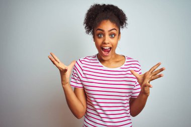 Afro-Amerikan kadın izole beyaz arka plan üzerinde rahat pembe çizgili t-shirt giyen deli kutluyor ve kollarını kaldırdı ve açık gözleri heyecan çığlık ile başarı için hayran. Kazanan kavramı