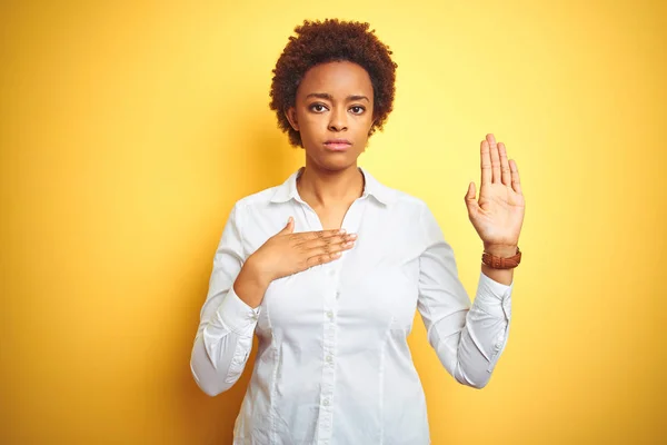 African american business woman over isolated yellow background Swearing with hand on chest and open palm, making a loyalty promise oath