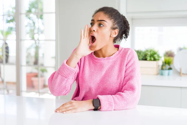 Afro saçlı güzel afro-amerikan kadın rahat pembe kazak giyen bağırarak ve ağızda el ile yan yüksek sesle bağırıyor. İletişim kavramı.