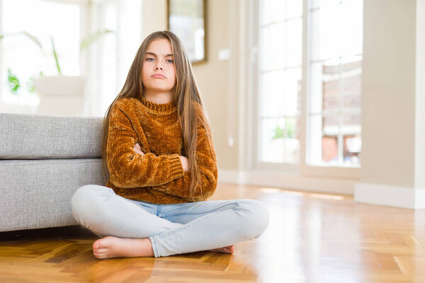 Beautiful young girl kid sitting on the floor at home skeptic and nervous, disapproving expression on face with crossed arms. Negative person.