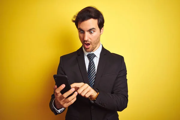 Молодой Красивый Бизнесмен Используя Смартфон Стоящий Изолированном Желтом Фоне Напуганный — стоковое фото