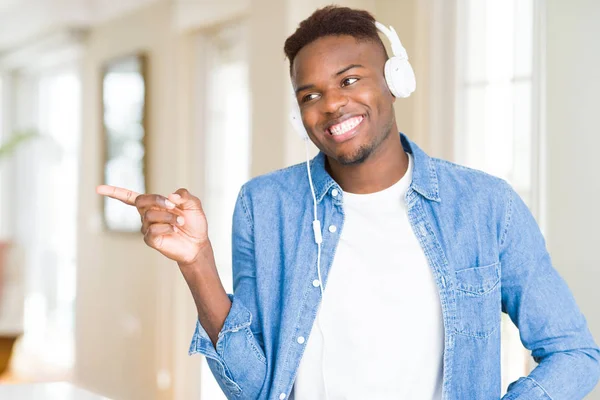 カメラを見て手と指で指を向け 笑顔で音楽を聴くヘッドフォンを着たアフリカ系アメリカ人男性 — ストック写真
