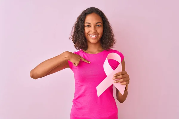 孤立したピンクの背景の上に立つ癌のリボンを持つ若いブラジルの女性は 自分自身に指を指差す驚きの顔を持つ — ストック写真