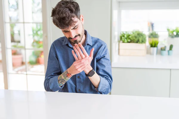 Young man wearing casual shirt sitting on white table Suffering pain on hands and fingers, arthritis inflammation