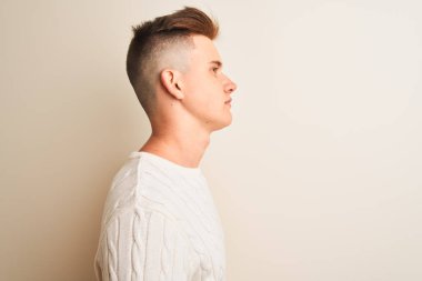 Yan bakan izole beyaz arka plan üzerinde duran kış kazak giyen genç yakışıklı adam, kendine güvenen gülümseme ile doğal yüzü ile profil poz rahatlayın.