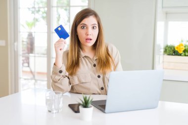 Güzel genç kadın alışveriş online dizüstü bilgisayar ve kredi kartı kullanarak sürpriz bir yüz ile şok korkmuş, korku ve korku ifade ile heyecanlı