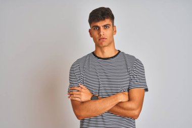 Izole beyaz arka plan şüpheci ve sinirli üzerinde duran lacivert çizgili t-shirt giyen genç Hintli adam, çapraz kolları ile yüzünde onaylamayan ifade. Negatif kişi.