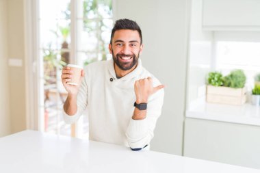Yakışıklı İspanyol adam bir kağıt fincan işaret bir kahve içme ve mutlu yüzü gülümseyerek yan başparmak ile gösteren