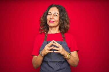 Orta yaş yaşlı kadın kırmızı izole arka plan eller üzerinde önlük üniforma giyen birlikte ve parmakları gülümseyerek rahat ve neşeli geçti. Başarı ve iyimser