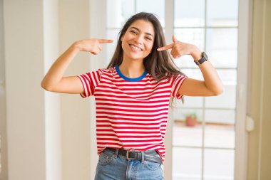 Kendinden emin gösterilen ve işaret parmakları diş ve ağız ile gülümseyen rahat t-shirt giyen genç güzel kadın. Sağlık kavramı.