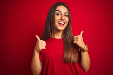 Genç güzel kadın izole kırmızı arka plan başarı işareti üzerinde duran t-shirt giyen el ile olumlu jest yapıyor, gülümseyen ve mutlu başparmak kadar. Neşeli ifade ve kazanan jest.