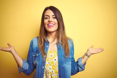 Genç güzel kadın sarı izole arka plan üzerinde duran gülümseyerek her iki elaçık avuç içi gösteren, sunan ve reklam karşılaştırma ve denge
