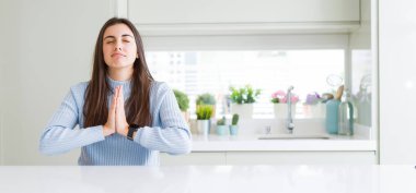 Evde beyaz masada oturan güzel genç kadının geniş açı resmi yalvarıyor ve yüz üzerinde umut ifade ile birlikte eller ile dua çok duygusal ve endişeli. Affedilmesini istiyorum. Din konsepti.