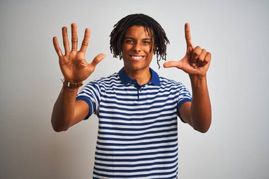 Çizgili mavi polo giyen dreadlocks giyen Afro adam izole beyaz arka plan üzerinde duran gösteren ve emin ve mutlu gülümserken parmakları sayısı yedi ile işaret.