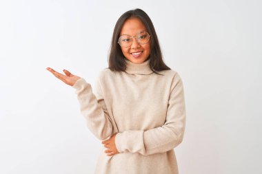 Genç çinli kadın boğazlı kazak ve gözlük izole beyaz arka plan üzerinde neşeli sunan gülümseyerek giyen ve kameraya bakarak avuç içi ile işaret.