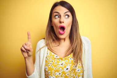Genç güzel kadın ceket giyen sarı izole arka plan üzerinde duran başarılı bir fikir ile parmak işaret. Çıktı ve mutlu. Bir numara.