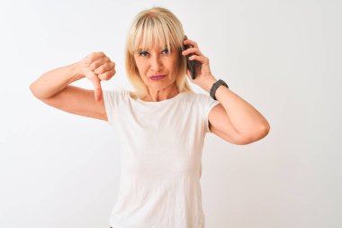 Orta yaş kadın kızgın yüz ile izole beyaz arka plan üzerinde duran akıllı telefon üzerinde konuşurken, başparmak aşağı ile sevmediğimi gösteren negatif işareti, ret kavramı