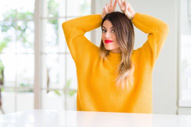 Evde kış kazak giyen genç güzel kadın komik ve çılgın baş parmaklar ile poz tavşan kulakları neşeli gülümseyen