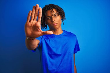 Afro amerikan adam dreadlocks giyen t-shirt izole mavi arka plan üzerinde duran avuç içi ile şarkı durdurmak yapıyor. Yüzünde olumsuz ve ciddi bir jest olan uyarı ifadesi.