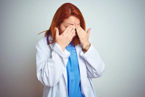 Young redhead doctor woman using stethoscope over white isolated background rubbing eyes for fatigue and headache, sleepy and tired expression. Vision problem