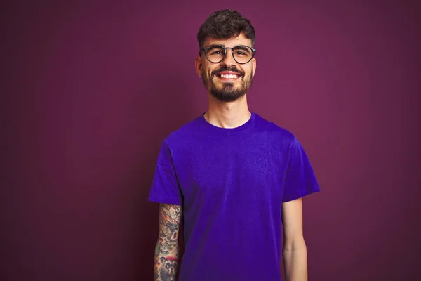 Tシャツとメガネをかけたタトゥーをした若い男は 顔に幸せでクールな笑顔で孤立した紫色の背景の上に立っています ラッキーな人 — ストック写真