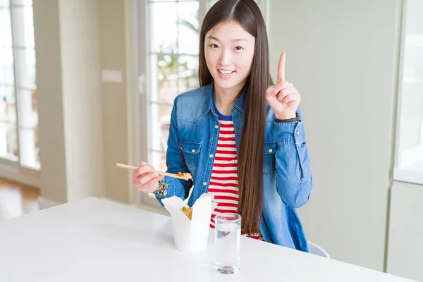 Beautiful Asian woman eating asian rice in delivery box surprised with an idea or question pointing finger with happy face, number one