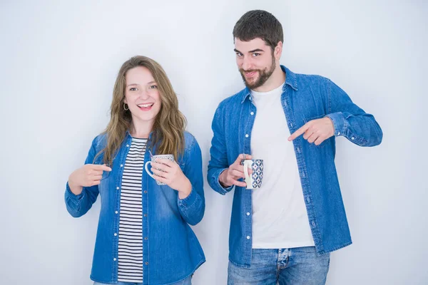 Genç güzel çift beyaz izole arka plan üzerinde bir fincan kahve içme çok mutlu el ve parmak ile işaret