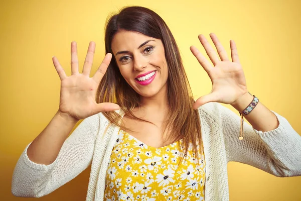 Genç güzel kadın sarı izole arka plan üzerinde duran ceket giyen gösteren ve emin ve mutlu gülümserken parmakları on numara ile işaret.