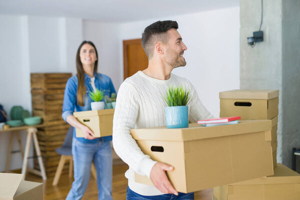 Молодая пара переезжает в новый дом, улыбаясь счастливо держа картонные коробки в новой квартире
