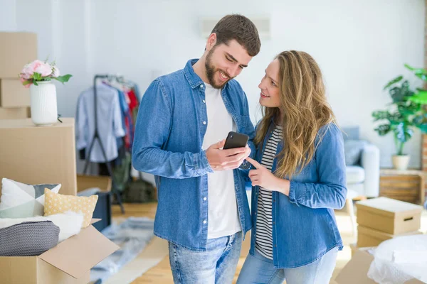 Genç çift karton kutular etrafında akıllı telefon kullanarak yeni bir eve hareket