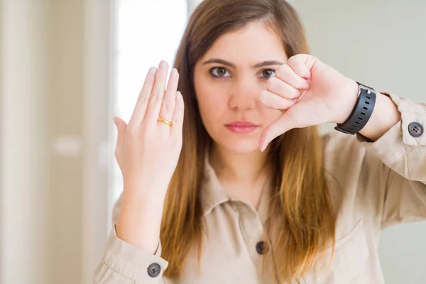 怒った顔で同盟指輪を手に見せる美しい若い女性 親指を下して嫌いを示すネガティブサイン 拒絶概念 — ストック写真