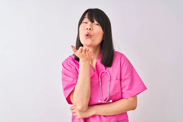 年轻漂亮的中国护士妇女穿着听诊器在孤立的白色背景看着相机吹一个吻与手在空中可爱和性感 爱表达 — 图库照片