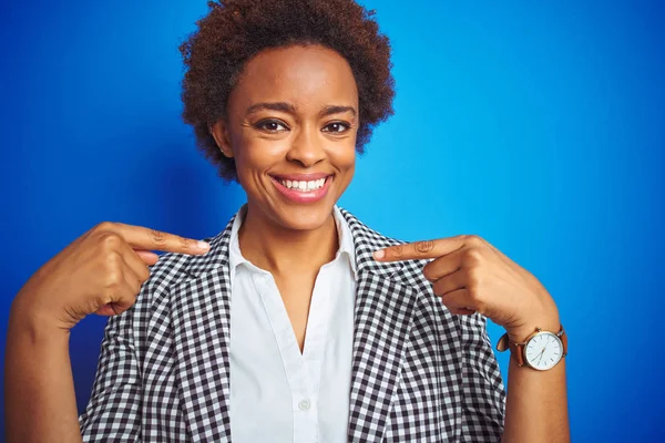 African american business executive woman over isolated blue background looking confident with smile on face, pointing oneself with fingers proud and happy.