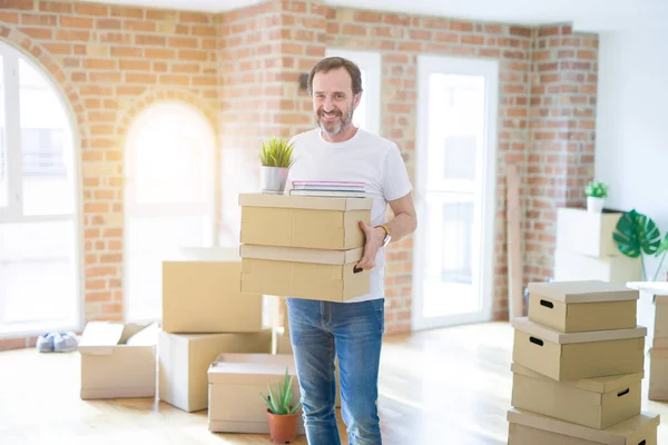 Handsome middle age senior man smiling happy moving to a new house, packing and holding cardboard boxes