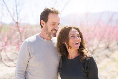 Baharın güneşli bir gününde pembe yaprakları ile şeftali ağaçlarının romantik bahçesinde aşık gülümseyen güzel orta yaş yaşlı çift