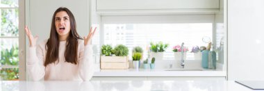 Evde beyaz masada oturan güzel genç kadının geniş açılı resmi deli ve deli bağırarak ve agresif ifade ve kollar kaldırdı ile bağırıyor. Hayal kırıklığı kavramı.