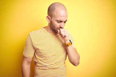 Sakalı olan genç kel adam sarı izole arka plan üzerinde rahat çizgili t-shirt giyen rahatsız hissediyorum ve soğuk veya bronşit için bir belirti olarak öksürük. Sağlık kavramı.